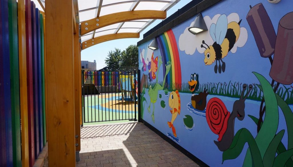 Wall of the Pond Nursery with a painted mural and a rainbow fence in front.